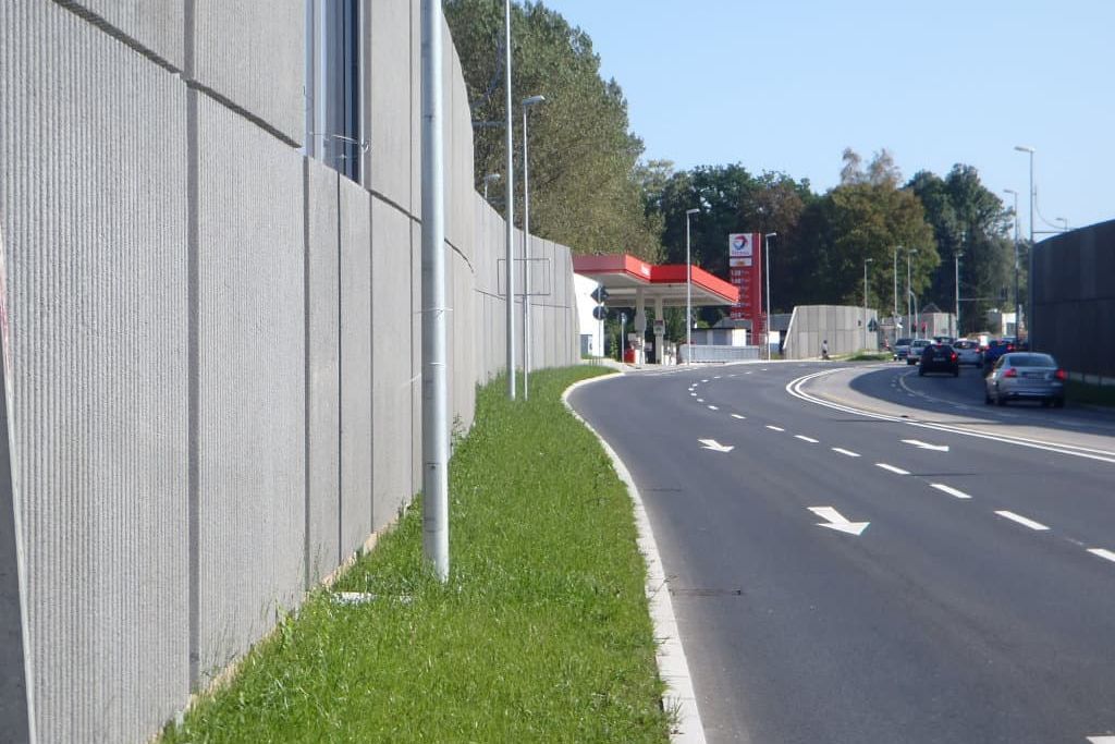 die fertige Zsqhopauerstraße mit Blick entlang des Geräuschschutzes einer Rasenbegremzung der Straße und einer Tankstelle