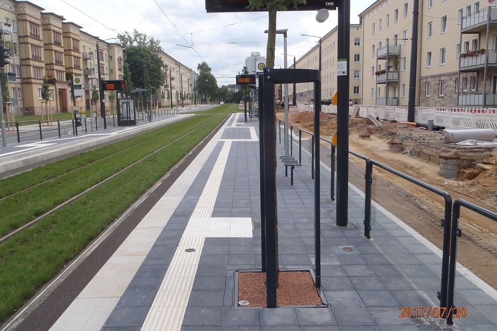 eine neue Bahnhaltestelle mit LED Anzeigetafeln für Zeiten für die Bahn begrenz von Schienen links und einer Baustelle einer Straße rechts