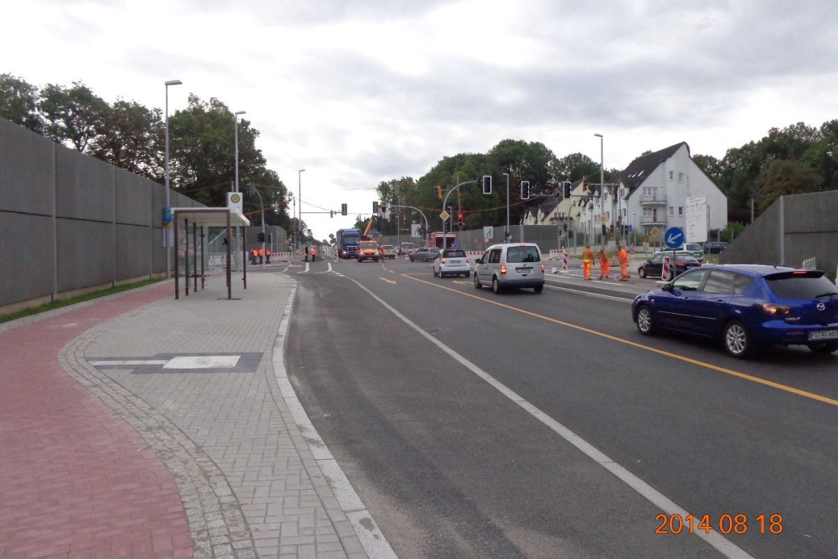 links ist ein Radweg und eine Bushaltestelle, mittig verläuft eine Straße welche Rechts von fahrenden Autos und danach von einer Baustelle begrenzt wird