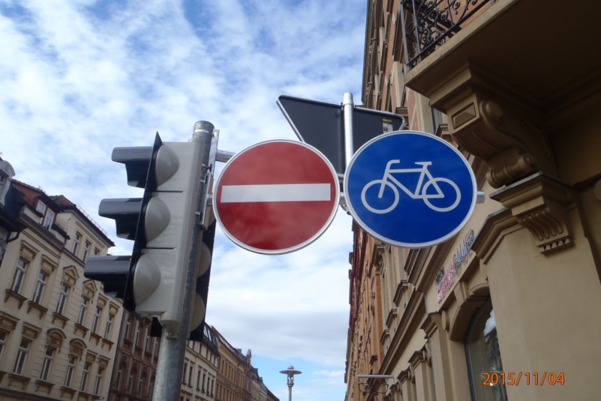 Eine Ampel, ein Straßenschild für Einbahnstraße und ein Straßenschild für Fahrräder erlaubt